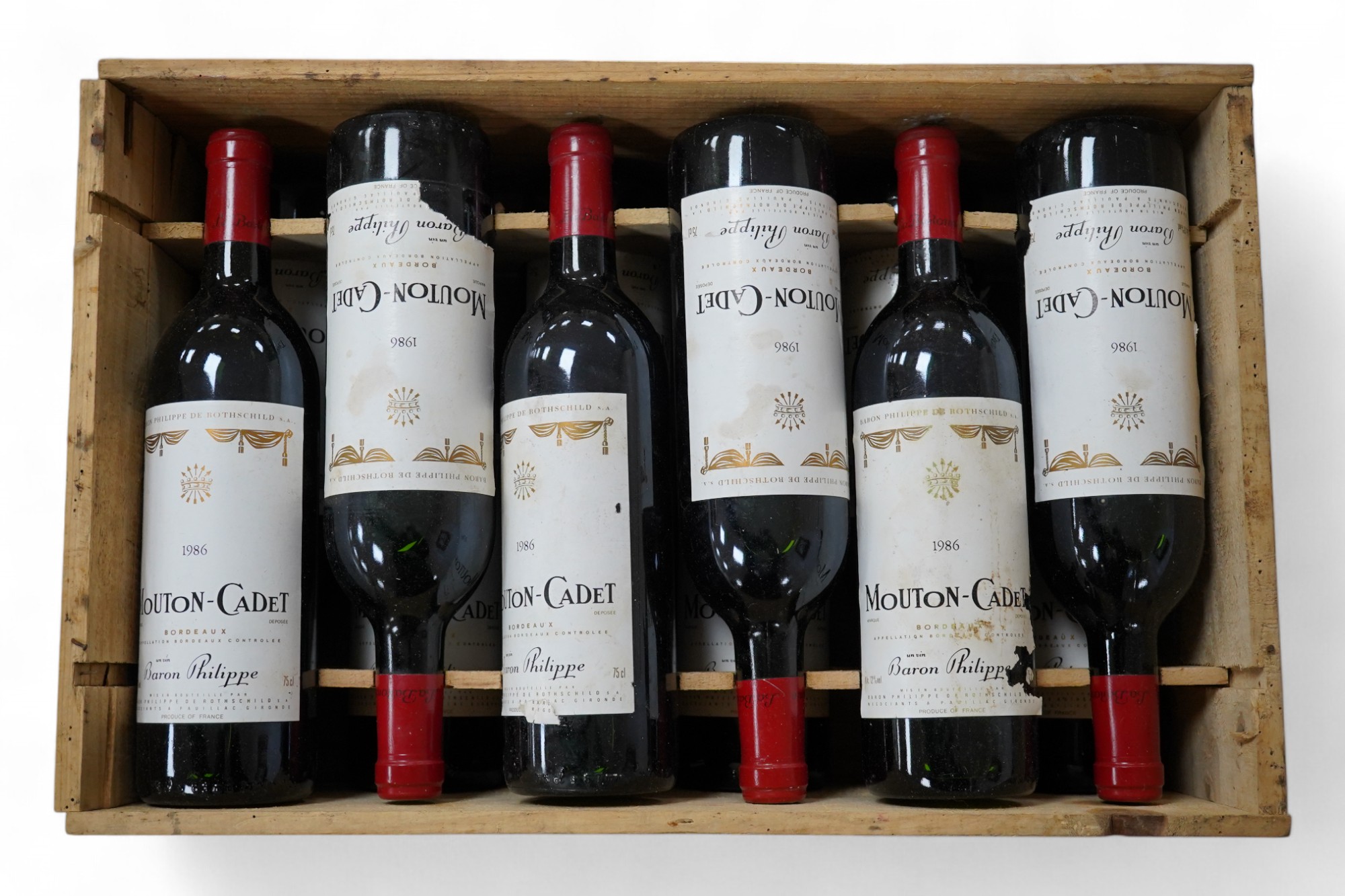 Twelve bottles of Mouton Cadet 1986 in associated wooden crate. Condition - wear to labels, storage unknown